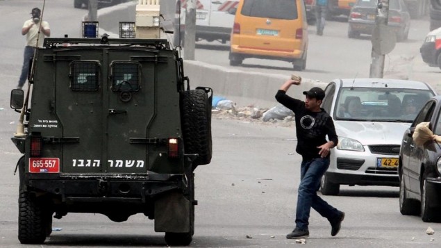 متظاهرون فلسطينيون يرشقون مركبة عسكرية اسرائيلية بالحجارة خلال مظاهرة عند مدخل حاجز قلنديا، 30 مارس 2013 (Issam Rimawi/Flash90)