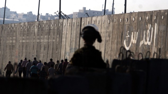 جندي اسرائيلي يراقب فلسطينيين يمرون حاجز قلنديا متجهين نحو القدس (Issam Rimawi/Flash90)
