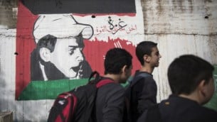 فتية في طريقهم إلى البيت من المدرسة يمرون إلى جانب رسم لمحمد أبو خضير، الفتى الفلسطيني الذي قُتل على يد متطرفين يهود، مع العلم الفلسطيني، في شارع مركزي شمال إسرائيل. (Hadas Parush/Flash90)