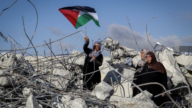 والدة مراد ادعيس، منفذ هجوم فلسطيني، تحمل العلم الفلسطيني خلال وقوفها على على أنقاض منزل العائلة بعد أن قام الجيش الإسرائيلي بهدمه في قرية يطا، جنوبي الخليل، في 11 يونيو، 2016. دعيس قام بقتل دفنا مئير، الأم لستة أطفال، بعد طعنها. والدة مراد ادعيس، منفذ هجوم فلسطيني، تحمل العلم الفلسطيني خلال وقوفها على على أنقاض منزل العائلة بعد أن قام الجيش الإسرائيلي بهدمه في قرية يطا، جنوبي الخليل، في 11 يونيو، 2016. دعيس قام بقتل دفنا مئير، الأم لستة أطفال، بعد طعنها.