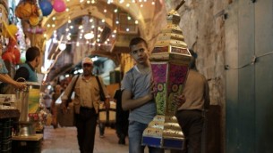 صورة توضيحية: طفل فلسطيين يحمل فانوسا يمر أمام محلات تجارية في البلدة القديمة بالقدس في 16 يونيو، 2015. (AFP PHOTO/AHMAD GHARABLI)