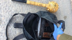 جندي إسرائيلي يتفقد سلاح رشاش من نوع ’كارلو’ تمت مصادرته خلال  عملية إحباط صفقة أسلحة، إلى جانب ما يبدو كصولجان خشبي، في حلحول، خارج الخليل، 6 أكتوبر، 2016. (IDF Spokesperson’s Unit)
