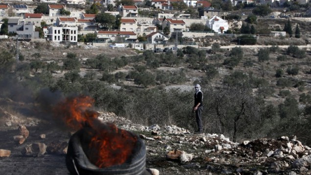 متظاهر فلسطيني ينظر الى اطارات مشتعلة خلال مواجهات مع قوات الامن الإسرائيلية بالقرب من مستوطنة كيدزميم في الضفة الغربية، 9 ديسمبر 2016 (AFP/JAAFAR ASHTIYEH)