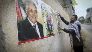 فلسطيني يلصق صورا للزعيم الفلسطيني الراحل ياسر عرفات ورئيس السلطة الفلسطينية محمود عباس، في مدينة نابلس في الضفة الغربية، 14 مارس، 2017. (Nasser Ishtayeh/Flash90)