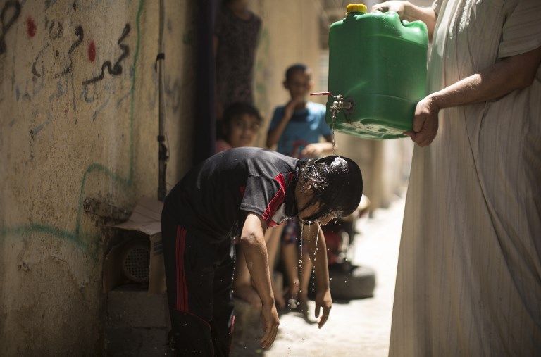 طفل فلسطيني يقوم بتبريد نفسه بماء من صفيحة يحملها رجل خلال موجة حر في مخيم الشاطئ في مدينة غزة، 2 يوليو، 2017. (AFP PHOTO / Mahmud Hams) طفل فلسطيني يقوم بتبريد نفسه بماء من صفيحة يحملها رجل خلال موجة حر في مخيم الشاطئ في مدينة غزة، 2 يوليو، 2017. (AFP PHOTO / Mahmud Hams)