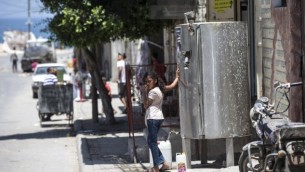 طفلة فلسطينية تملأ وعاء بالماء خلال موجة حر في مخيم الشاطئ في مدينة غزة، 2 يوليو، 2017. (AFP PHOTO / MAHMUD HAMS)