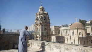 راهب أرثوذكسي في "دير الصليب" يحمل خرطوم مياه وهو يقف على  سقف الدير أثناء اندلاع حريق في ’وداي الصليب’، وسط القدس، 2 يوليو، 2013. (FLASH90)
