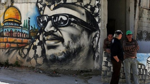يقف لاجئون فلسطينيون بجانب كتابات تحمل صورة لرئيس السلطة الفلسطينية الراحل ياسر عرفات في مخيم عين الحلوة للاجئين بالقرب من مدينة صيدا بجنوب لبنان في 16 مارس / آذار 2015. (AFP/Joseph Eid)
