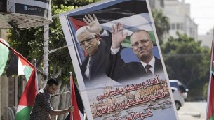صاحب متجر فلسطيني يعرض أعلاما فلسطينية وملصق يحمل صورة رئيس الوزراء الفلسطيني راي الحمد الله ورئيس السلطة الفلسطينية محمود عباس، 1 أكتوبر، 2017، في مدينة غزة. (AFP PHOTO/MAHMUD HAMS)