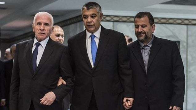 رئيس جهاز المخابرات المصرية خالد فوزي، وسط الصورة، يصل برفقة المسؤول في حركة ’فتح’ عزام الأحمد، من اليسار، والمسؤول في ’حماس’ صالح العاروري، من اليمين، قبل التوقيع  على اتفاق المصالحة في القاهرة في 12 أكتوبر، 2017. (AFP/ KHALED DESOUKI)