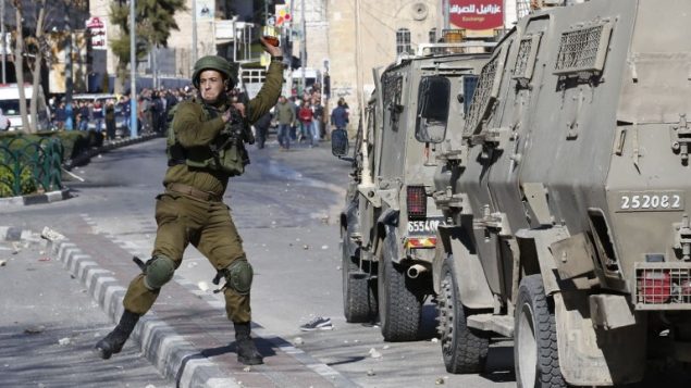جندي اسرائيلي يلقي قنبلة صوت باتجاه متظاهرين فلسطينيين خلال مواجهات في الخليل، 8 ديسمبر 2017 (Hazem Bader/AFP)