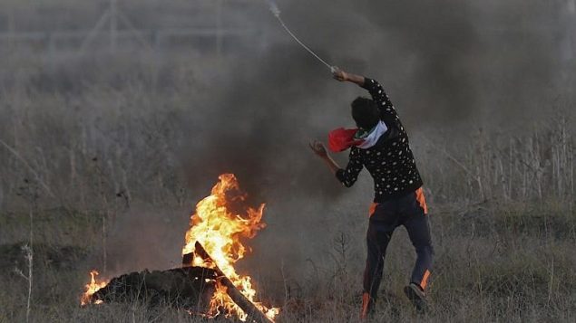 محتج فلسطيني يلقي بحجر اتجاه القوات الإسرائيلية خلال مواجهات على الحدود بين إسرائيل وغزة شرقي مدينة غزة في 9 ديسمبر، 2017،  في أعقاب قرار الرئيس الأمريكي دونالد ترامب الإعتراف بالقدس عاصمة لإسرائيل. (AFP/Mahmud Hams)