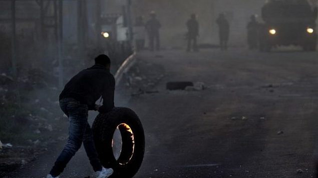متظاهر فلسطيني يدفع بإطار مشتعل باتجاه القوات الإسرائيلية خلال مواجهات في مدينة نابلس في الضفة الغربية، في 9 ديسمبر، 2017، في أعقاب تظاهرات ضد قرار الرئيس الأمريكي دونالد ترامب الإعتراف بالقدس عاصمة لإسرائيل. (AFP PHOTO/ AAFAR ASHTIYEH)