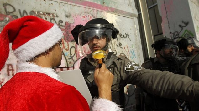 متظاهر فلسطيني يرتدي بدلة سانتا كلوز يواجه شرطي حرس حدود إسرائيل خلال تظاهرة عند المدخل الرئيسي لمدينة بيت لحم، 23 ديسمبر، 2017. (AFP PHOTO / Musa AL SHAER)