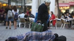 مارة يسيرون من أمام رجل مشرد ينام في الشارع، بالقرب من المقاهي في وسط مدينة القدس 10 نوفمبر، 2013. (Nati Shohat/FLASH90)