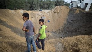 صورة توضيحية: يقف أطفال فلسطينيون بالقرب من حفرة في بيت لاهيا في شمال قطاع غزة في 22 أغسطس / آب 2016، بعد غارة جوية إسرائيلية استهدفت مواقع حماس ردا على صاروخ أطلق من القطاع الذي ضرب مدينة سديروت الإسرائيلية. (Mahmud Hams/AFP)