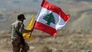 عنصر من منظمة حزب الله يحمل العلم اللبناني وعلم حزب الله خلال جولة لوسائل الإعلام بالقرب من بلدة عرسال الحدودية في 25 يوليو، 2017.   (AFP Photo/Stringer)