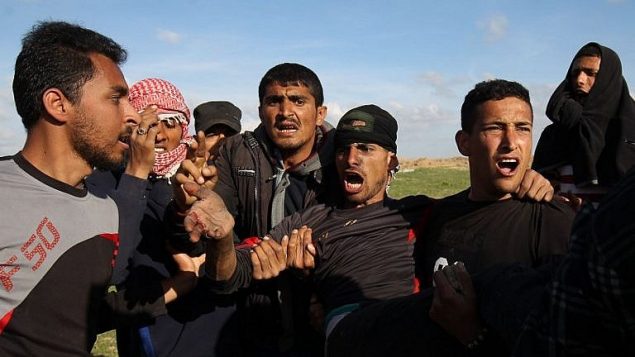 رجال فلسطينيون يحملون متظاهر مصاب خلال اشباكات مع جنود اسرائيليين بالقرب من السياج الحدودي في جنوب قطاع غزة، 16 مارس 2018 (AFP Photo/Said Khatib)