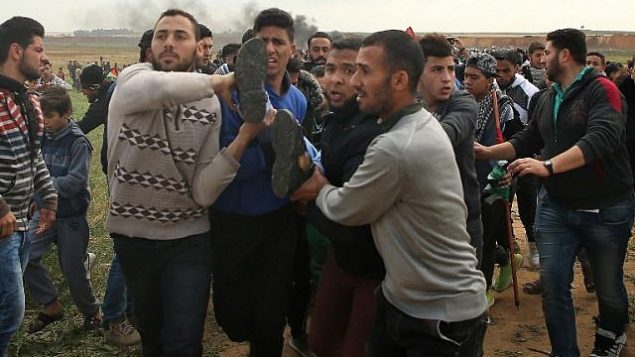 متظاهرون يحملون فلسطيني مصاب اثناء الفرار خلال اشتباكات في مظاهرة بالقرب من الحدود مع اسرائيل شرقي مدينة غزة في يوم الارض، 30 مارس 2018 (AFP/ Mohammed ABED) متظاهرون يحملون فلسطيني مصاب اثناء الفرار خلال اشتباكات في مظاهرة بالقرب من الحدود مع اسرائيل شرقي مدينة غزة في يوم الارض، 30 مارس 2018 (AFP/ Mohammed ABED)