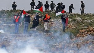 رجال فلسطينيون يرفعون الأعلام أمام القوات الإسرائيلية خلال مظاهرة تخلد ذكرى يوم الأرض في قرية كسرى بالضفة الغربية في 30 مارس / آذار 2018. (AFP/Jaafar Ashtiyeh)