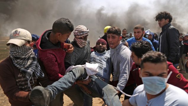 رجال فلسطينيون يحملون متظاهر مصاب خلال اشتباكات مع القوات الإسرائيلية امام الحدود بين غزة واسرائيل، شرقي مدينة غزة، 6 ابريل 2018 (MAHMUD HAMS / AFP)