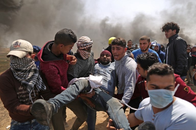 رجال فلسطينيون يحملون متظاهر مصاب خلال اشتباكات مع القوات الإسرائيلية امام الحدود بين غزة واسرائيل، شرقي مدينة غزة، 6 ابريل 2018 (MAHMUD HAMS / AFP)