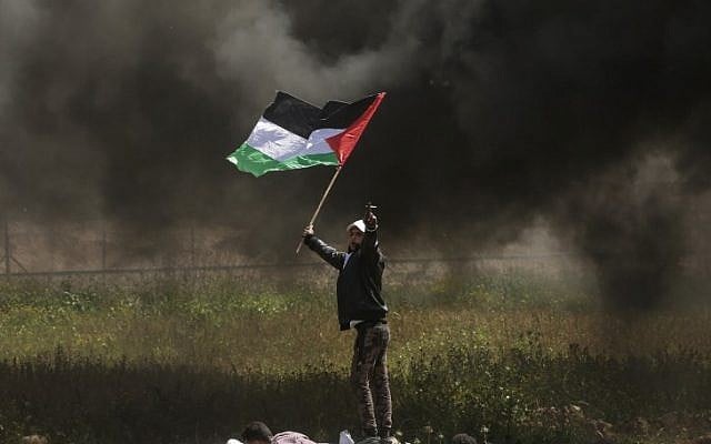 أحد المتظاهرين الفلسطينيين يلوح بعلمه الوطني خلال اشتباكات مع قوات الأمن الإسرائيلية على الحدود بين غزة وإسرائيل، شرق مدينة غزة في 6 أبريل، 2018. (AFP PHOTO / MAHMUD HAMS)