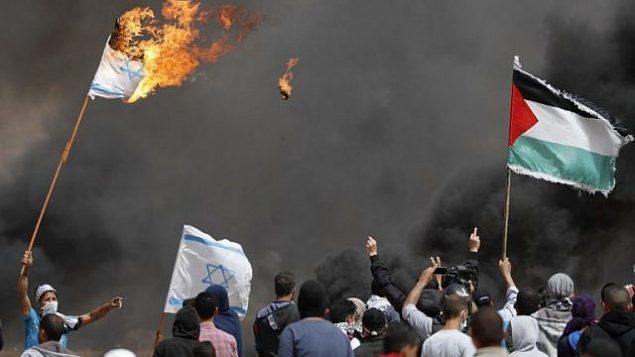 محتجون فلسطينيون يحرقون الأعلام الإسرائيلية بالقرب من السياج الحدودي مع إسرائيل، شرق خان يونس في جنوب مدينة غزة، في 13 أبريل 2018. (AFP/Thomas Coex)