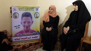 والدة الطفل الفلسطيني (وسط الصورة) البالغ من العمر 15 عاما والذي قُتل بحسب تقارير بنيران الجيش الإسرائيلي خلال مواجهات عند السياج الحدودي بين غزة وإسرائيل، تجلس إلى جانب شخص آخر يرفع صورته، في منزل العائلة في بيت لاهيا في شمال قطاع غزة في 21 أبريل، 2018.  (AFP PHOTO / MAHMUD HAMS).