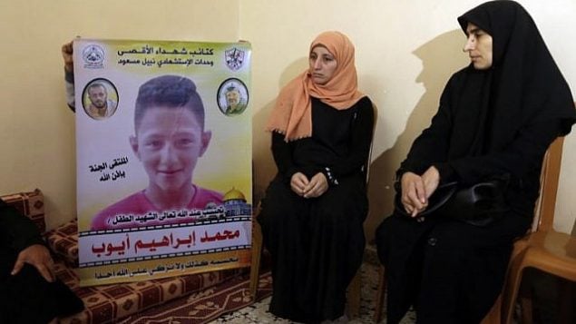 والدة الطفل الفلسطيني (وسط الصورة) البالغ من العمر 15 عاما والذي قُتل بحسب تقارير بنيران الجيش الإسرائيلي خلال مواجهات عند السياج الحدودي بين غزة وإسرائيل، تجلس إلى جانب شخص آخر يرفع صورته، في منزل العائلة في بيت لاهيا في شمال قطاع غزة في 21 أبريل، 2018.  (AFP PHOTO / MAHMUD HAMS).