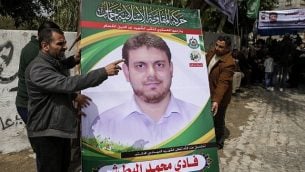 صورة تم التقاطها في 21 أبريل، 2018 تظهر رجالا يرفعون ملصقا يحمل صورة  صورة البروفسور والعضو في حركة حماس، فادي محمد البطش (35 عاما) الذي قُتل في وقت سابق من اليوم في ماليزيا، خارج منزل عائلته في جباليا شمال الضفة الغربية. ( AFP PHOTO / MAHMUD HAMS)