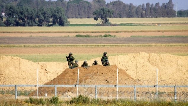 جنود إسرائيليون يراقبون محتجين فلسطينيين في أعقاب مظاهرة بالقرب من السياج الحدودي مع إسرائيل، شرقي خان يونس، في جنوب قطاع غزة، 1 أبريل، 2018. (Abed Rahim Khatib/ Flash90)