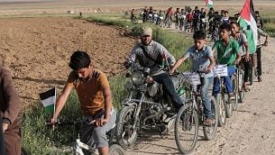أطفال فلسطينيون يركبون الدراجات بالقرب من الحدود مع إسرائيل في ضواحي مدينة خان يونس في جنوب قطاع غزة، خلال مشاركتهم في سباق دراجات للمطالبة ب’حق العودة’ لملايين الفلسطينيين إلى إسرائيل، 26 مارس، 2018. (AFP/Said Khatib)