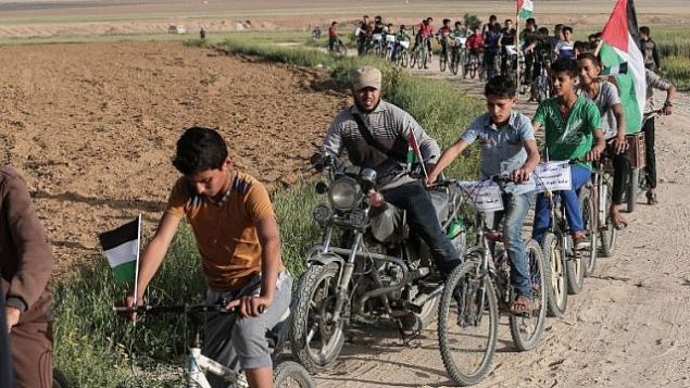 أطفال فلسطينيون يركبون الدراجات بالقرب من الحدود مع إسرائيل في ضواحي مدينة خان يونس في جنوب قطاع غزة، خلال مشاركتهم في سباق دراجات للمطالبة ب’حق العودة’ لملايين الفلسطينيين إلى إسرائيل، 26 مارس، 2018. (AFP/Said Khatib)