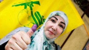 امراة شيعية لبنانية تعرض ابهامها الملون بالحبر وتلوح بعلم حزب الله بعد التصويت في محطة اقتراع في العاصمة بيروت في 6 مايو، 2018، في اليوم الذي تجري فيه البلاد انتخابات برلمانية لأول مرة منذ تسع سنوات. (AFP PHOTO / ANWAR AMRO)
