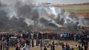 متظاهرون فلسطينيون ينظرون إلى الغاز المسيل للدموع والدخان المتصاعد من إطارات محترقة، شرقي مدينة غزة في 14 مايو، 2018. 
(AFP PHOTO / Mohammed ABED)