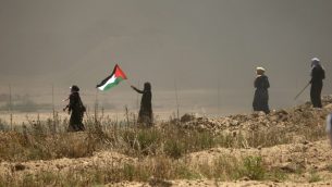 نساء فلسطينيات يوحن بالعلم الفلسطيني خلال مواجهات مع القوات الإسرائيلية بالقرب من الحدود بين قطاع غزة وإسرائيل، شرقي مدينة غزة، 14 مايو، 2018.  (AFP PHOTO / MAHMUD HAMS)