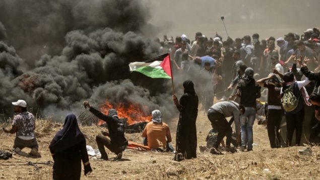 امرأة من غزة تحمل العلم الفلسطيني امام  اشتباكات بين فلسطينيين والجيش الإسرائيلي بالقرب من الحدود بين قطاع غزة وإسرائيل  14 مايو / أيار 2018 يوم تدشين السفارة الأمريكية في القدس MAHMUD HAMS / AFP