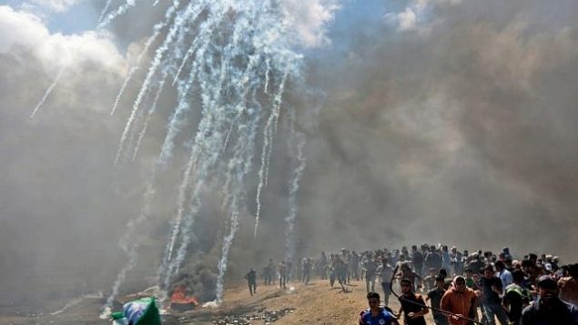 فلسطينيون يحاولون الاختباء من الغاز المسيل للدموع الذي أطلقته القوات الإسرائيلية بالقرب من الحدود بين قطاع غزة وإسرائيل في شرقي مدينة غزة، 14 مايو، 2018. (AFP/ MAHMUD HAMS)