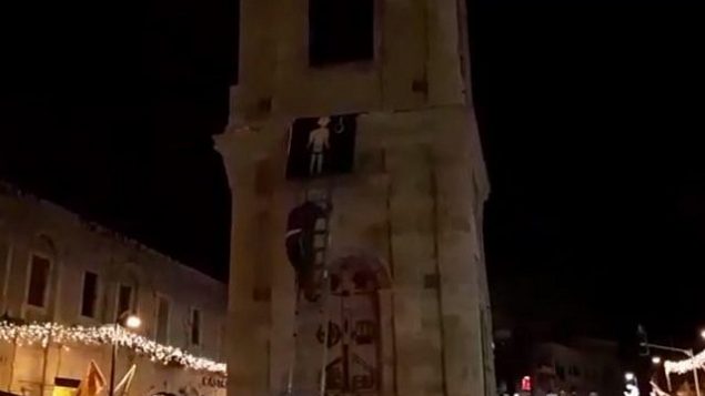 ناشطان من منظمة ’عوتسما يهوديت’ يقومون بتعليق صورة لمنفذ هجوم على برج الساعة في يافا.  (لقطة شاشة: Ynet news)