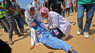 رزان النجار (من اليمين)، مسعفة فلسطينية تبلغ من العمر 21 عاما تقدم الإسعاف لإحدى زميلاتها التي أصيبت خلال مواجهات بالقرب من الحدود مع إسرائيل، شرقي خان يونس في جنوب قطاع غزة، 15 مايو، 2018.  (AFP/ SAID KHATIB)