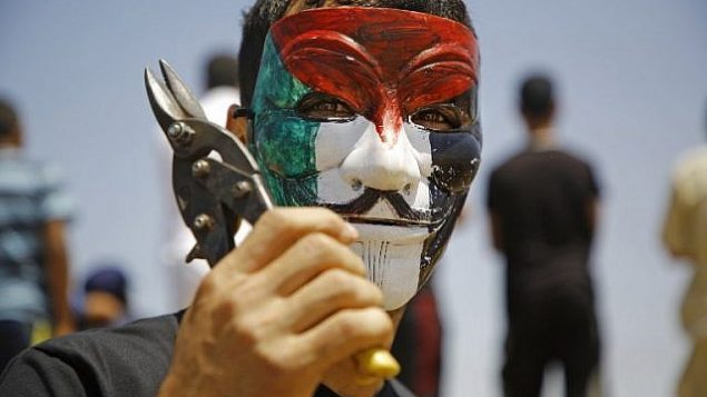 شاب فلسطيني يرتدي قناع جاي فوكس ملوناً بالعلم الفلسطيني يلوح بالمقصات خلال مظاهرة حاشدة على امتداد السياج الحدودي شرق جباليا في وسط قطاع غزة في 8 يونيو / حزيران 2018. (Said Khatib/AFP)
