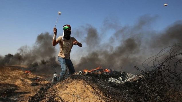 شاب فلسطيني يستخدم مقلاع لإلقاء الحجارة على القوات الإسرائيلية خلال اشتباكات قرب الحدود مع إسرائيل، شرق خان يونس في جنوب قطاع غزة في 8 يونيو  2018. (Said Khatib/AFP)