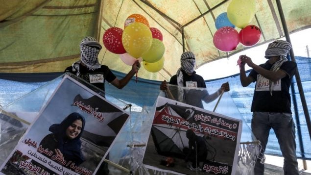 محتجون فلسطينيون يعدون بالونات محملة بمواد حارقة لإطلاقها باتجاه إسرائيل، عند حدود غزة إسرائيل في البريج، وسط قطاع غزة، 14 يونيو، 2018.  (AFP/Mahmud Hams)