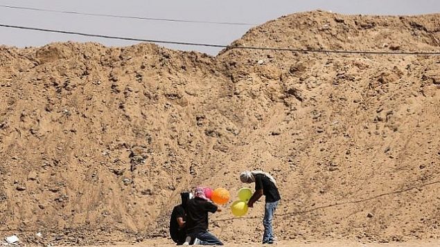 غزيون يعدون بالونات محملة بمواد حارقة لإطلاقها باتجاه إسرائيل، عند حدود غزة في البريح بوسط قطاع غزة، 14 يونيو، 2018. (AFP/ MAHMUD HAMS)