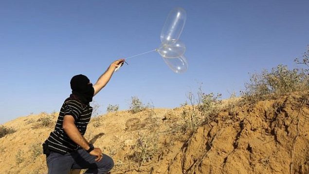 ملثم فلسطيني يطلق بالونا محملا بمواد حارقة باتجاه إسرائيل من مدينة رفح في جنوب قطاع غزة في 17 يونيو، 2018. (AFP Photo/Said Khatib) ملثم فلسطيني يطلق بالونا محملا بمواد حارقة باتجاه إسرائيل من مدينة رفح في جنوب قطاع غزة في 17 يونيو، 2018. (AFP Photo/Said Khatib)