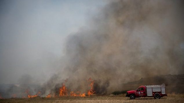 رجال الإطفاء يعملون على إخماد النار في حقل بعد اندلاع حريق فيه ناجم عن طائرات ورقية أطلقها فلسطينيون في قطاع غزة، بالقرب من الحدود مع قطاع غزة، 5 يونيو، 2018. (Yonatan Sindel/Flash90)