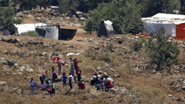 صورة تم التقاطها في 17 يوليو، 2018 من هضبة الجولان تظهر لاجئين يقتربون من السياج الحدودي بين سوريا وإسرائيل من مخيم للنازحين السوريين بالقرب من بلدة بريقة السورية في محافظة القنيطرة الجنوبية. (AFP /JALAA MAREY) صورة تم التقاطها في 17 يوليو، 2018 من هضبة الجولان تظهر لاجئين يقتربون من السياج الحدودي بين سوريا وإسرائيل من مخيم للنازحين السوريين بالقرب من بلدة بريقة السورية في محافظة القنيطرة الجنوبية. (AFP /JALAA MAREY)