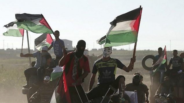 متظاهر فلسطيني يرتدي قناع غاي فوكس ويحمل علمه الفلسطيني خلال مظاهرة على طول الحدود بين إسرائيل وقطاع غزة، شرق مدينة غزة في 27 يوليو، 2018. (AFP PHOTO / MAHMUD HAMS) متظاهر فلسطيني يرتدي قناع غاي فوكس ويحمل علمه الفلسطيني خلال مظاهرة على طول الحدود بين إسرائيل وقطاع غزة، شرق مدينة غزة في 27 يوليو، 2018. (AFP PHOTO / MAHMUD HAMS)