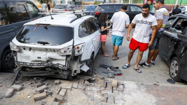 رجال اسرائيليون يقفون بجانب سيارة تضررت نتيجة قوط صاروخ اطلق من قطاع غزة في بلدة سديروت الإسرايلية في جنوب اسرائيل، 9 اغسطس 2018 (AFP PHOTO / JACK GUEZ)